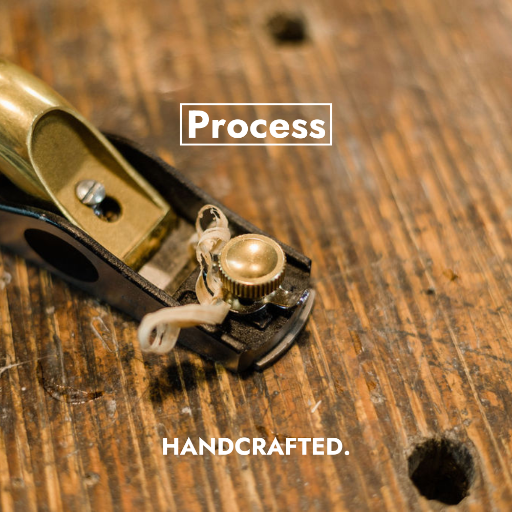 A handplane sits on a workbench at the Deviate Board Building shop with a fresh wood shaving sitting nearby.